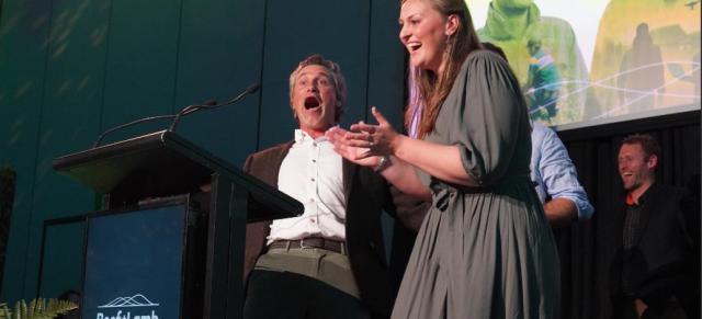 A man and woman stand at a podium with a microphone at the B+LNZ Awards ceremony.