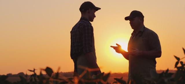 image of younger male talking to older farmer in the sunset