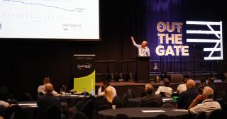 image of speaker pointing at screen at conference