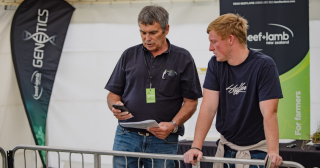 image of two mean at expo leaning over gate with cellphone