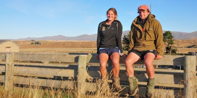 image of young male and female farmers sitting on fence