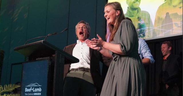 A man and woman stand at a podium with a microphone at the B+LNZ Awards ceremony.